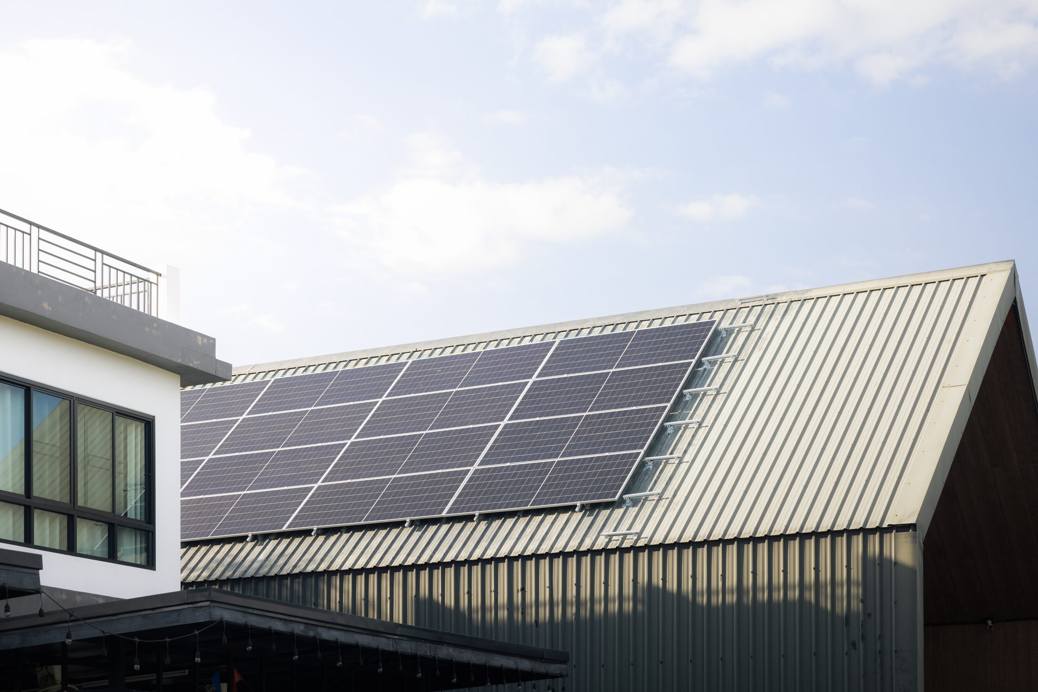 Solar panels installed on a building's corrugated metal roof under a partly cloudy sky.